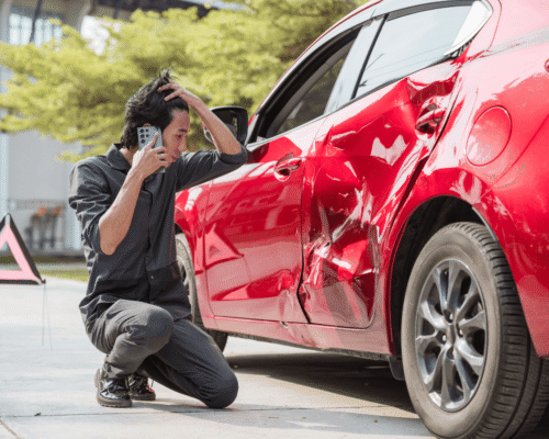 Man on his phone kneeling beside a red car with severe side damage after a crash, representing the importance of private investigations and expert crash reconstructions in Omaha accident cases when police reports may overlook key evidence.