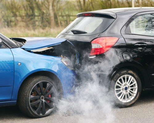 Two vehicles involved in a rear-end collision show significant damage and smoke at the crash scene, illustrating an uninsured motorist accident and insurance claim.