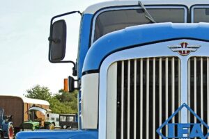 Blue and White big rig truck windshield featuring the mirror and grill.