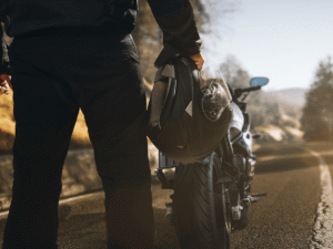 Motorcyclist holding helmet beside bike
